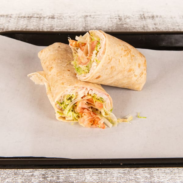 Two halves of a shrimp wrap, filled with lettuce, tomatoes, and onions, on parchment paper.