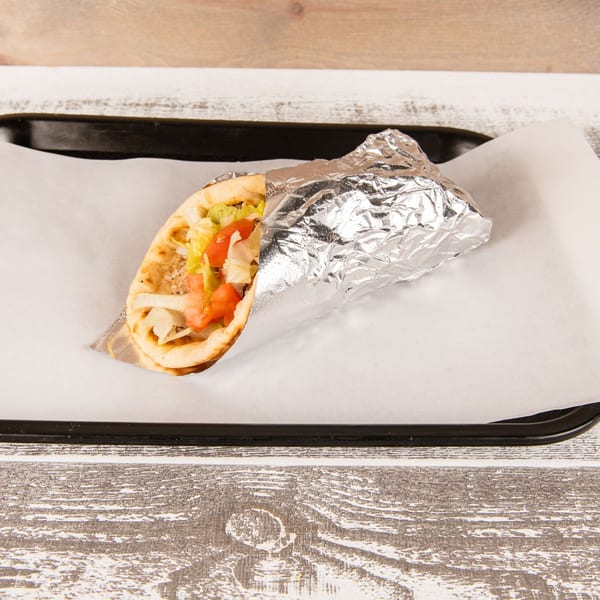 A gyro sandwich, partially wrapped in foil, filled with meat, lettuce, tomatoes, and onions on a tray.