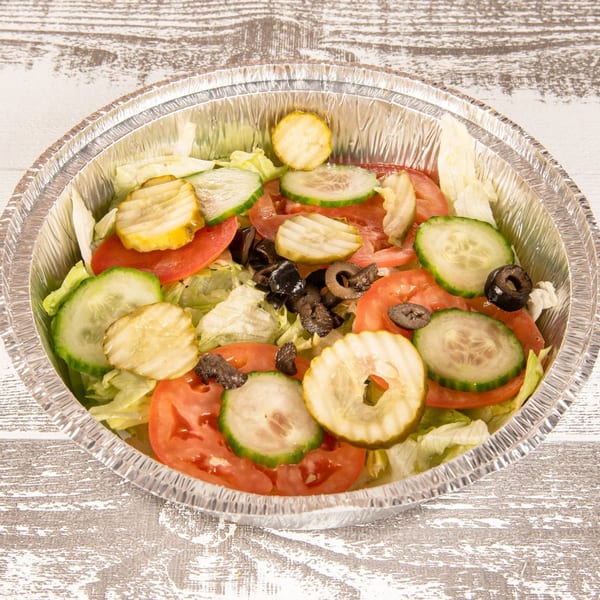 Fresh salad in a foil container with lettuce, tomatoes, cucumbers, pickles, and black olives.