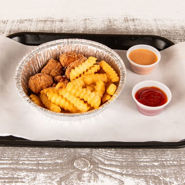Chicken nuggets and crinkle-cut fries in a foil bowl with ketchup and sauce on a tray.