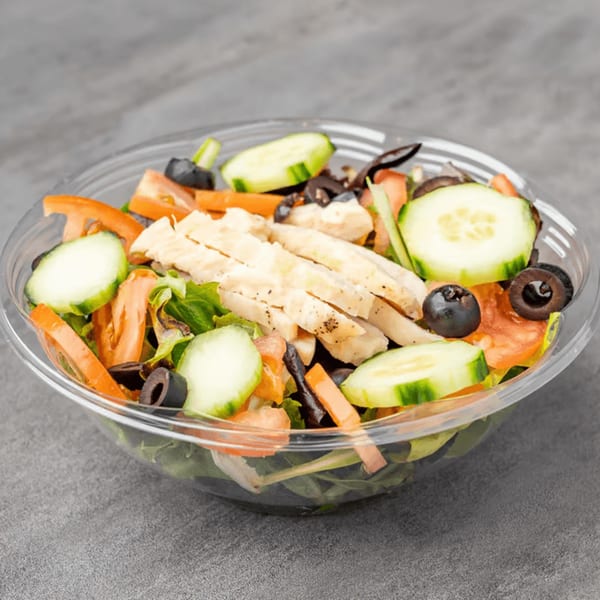 Fresh salad with sliced chicken, cucumbers, tomatoes, and black olives in a clear plastic bowl.