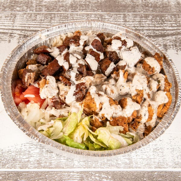 A foil container filled with rice, chicken, beef, lettuce, tomatoes, onions, and white sauce.